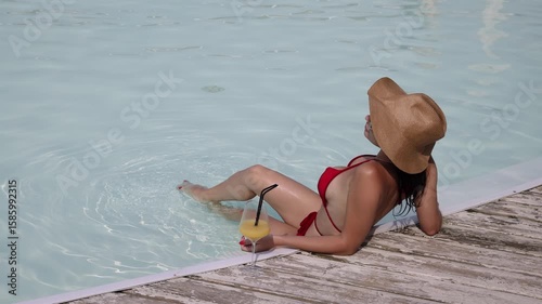 Beautiful woman in a hat enjoying relaxation in the pool with a cocktail. Concept leisure, summer vibes, calm and refreshment.