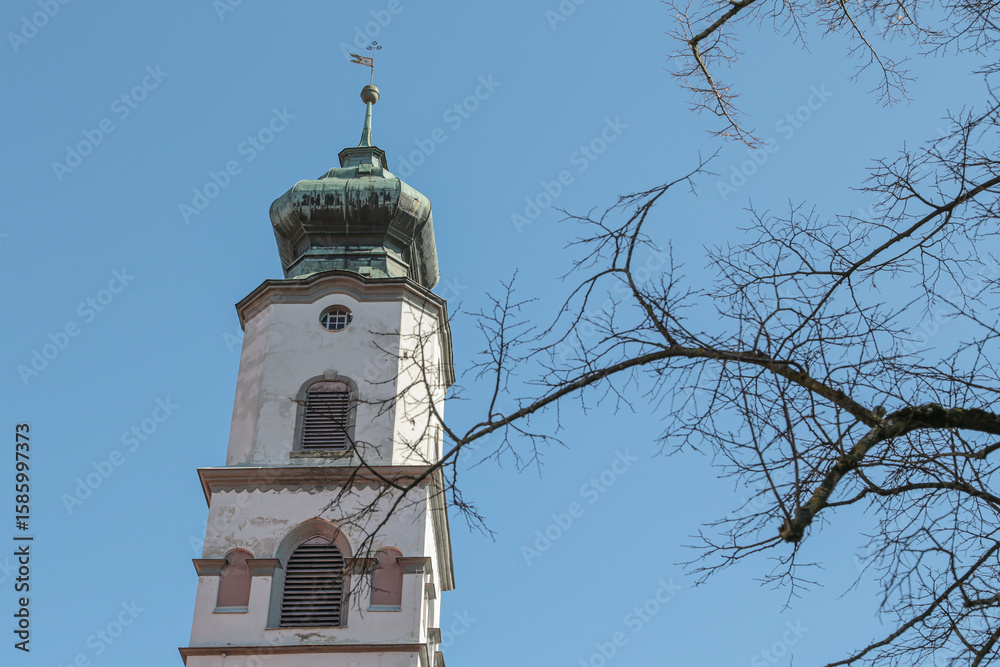 Fototapeta premium White church tower with a dome on top in Lindau, Germany An iron flag hangs on top On the right in the photo you can see a tree without leaves