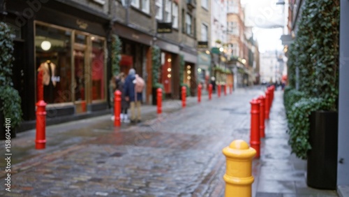 Canvas Print Blurry winter scene of a london street with red bollards, wet cobblestones, and indistinctly visible people, capturing the essence of an english autumn atmosphere in the united kingdom