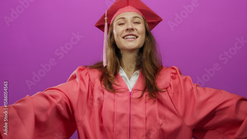 Bild auf Leinwand Young woman in graduation attire smiling confidently against a vibrant pink background, embodying a sense of achievement and joy