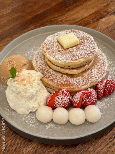 Delicious pancakes served on a plate, with butter, ice-cream, strawberries and glutinous rice balls.