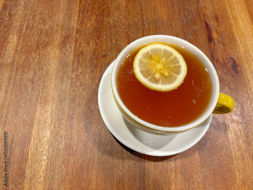 A full cup of English tea, with a slice of lemon floating on top. On a wooden table.