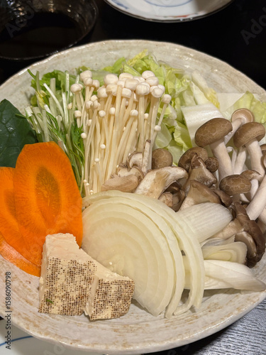 Closeup of a plate of raw vegetables and mushrooms, suitable to be used in Asian cuisine such as hotpot, shabu-shabu, nabe or sukiyaki.