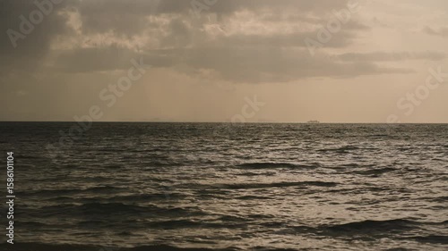Sunrays breaking through heavy storm clouds over the ocean with silhouetted rocky outcrop in distance creating intense mood wide angle shot Dramatic Weather Concept