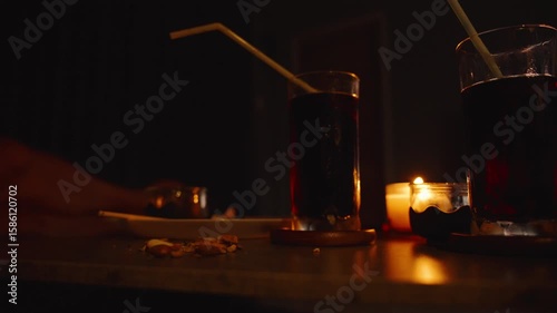 Fingers Picking Mixed Nuts on Table with Two Glasses of Dark Drinks and Candlelight While Watching TV low angle Relaxed TV Time Concept