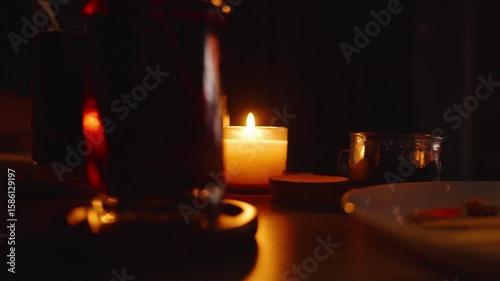 Glass of Dark Drink With Candle Flame Behind on Table and Plate With Food in Cozy Dim Room close up Relaxed TV Time Concept