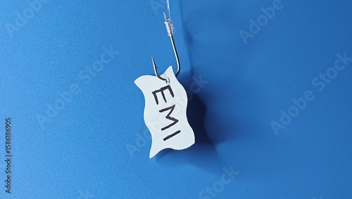 EMI word written on a paper and hooked on a fishing hook like lure. Isolated with blue background. loan repay, debt accumulation, payment crisis, liability, finance burden and payout struggle concept.