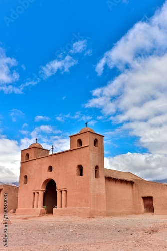 Vertical view of the Church of the Rosary in Andacollo, Catamarca, Argentina, with its adobe architecture, bell towers and crosses, under a blue sky with white clouds.