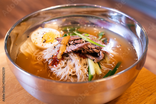 Korean cold beef noodle soup in metal bowl – front view