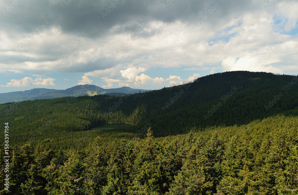 Obraz premium Sunlit Forested Mountains in Czech Republic Under Dramatic Clouds