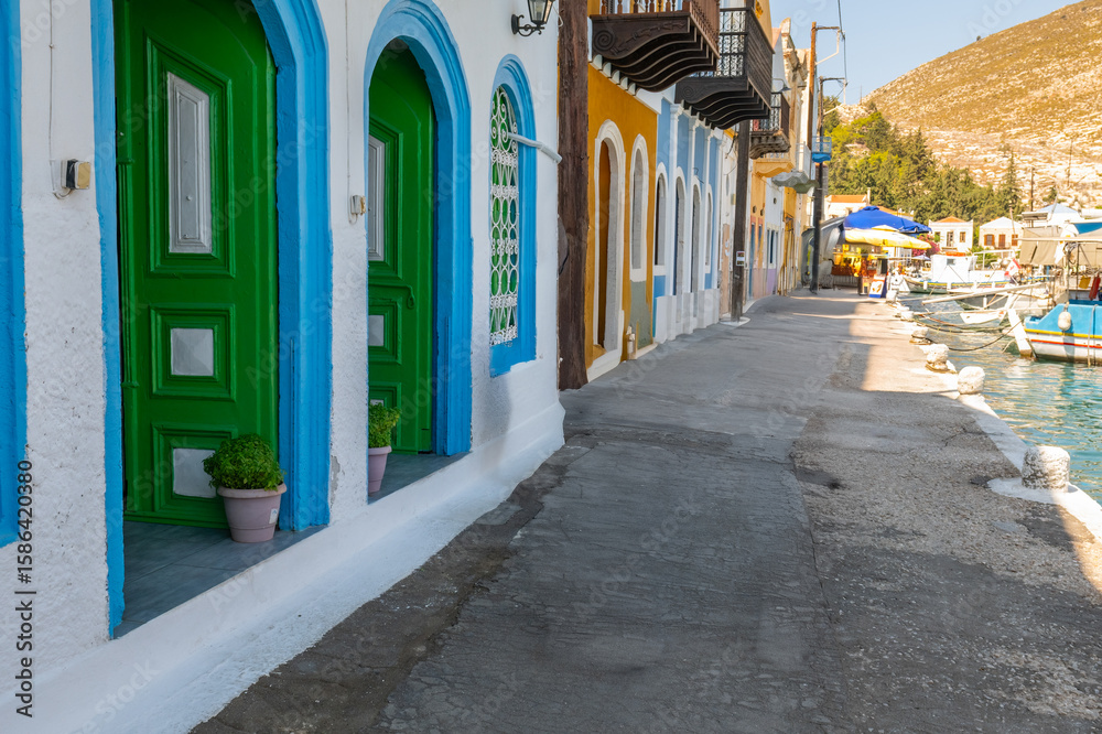 Fototapeta premium This photograph, which reflects the vibrant scenery of Meis Island, depicts a charming coastal street decorated with colorful doors and windows. Mediterranean architecture is an ideal choice for image
