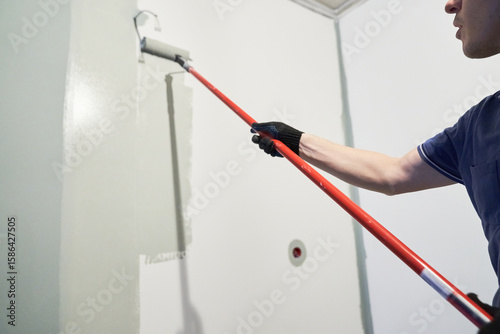 A worker paints the inner wall of his house. Apartment renovation. Concrete walls are painted gray with a paint roller. High quality photo