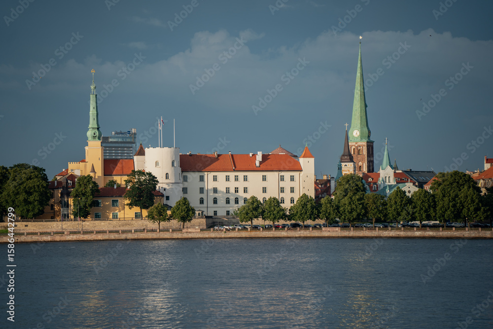 Fototapeta premium Historic Riga town skyline with church spires towers and castle reflecting in calm river water under clear blue sky on a sunny day urban architecture and cultural heritage cityscape