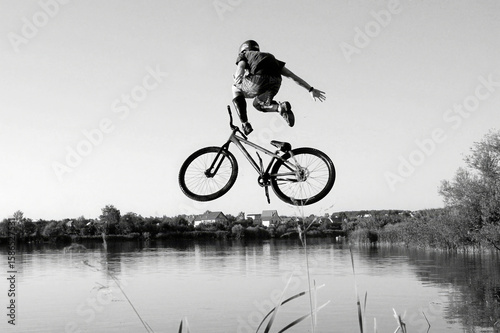 Принти на полотні Black and white photo of a person performing a high jump with a bicycle over a river