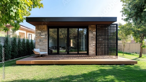 A modern outbuilding with a deck, glass doors, and brick accents nestled in lush greenery