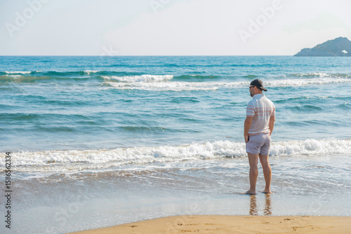 The man stands facing the sea and looks into the distance.