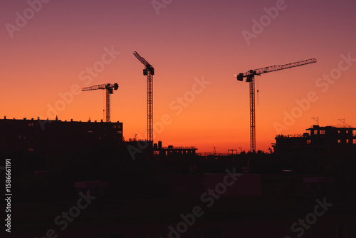 Construction Cranes Silhouetted at Sunset over a City Skyline