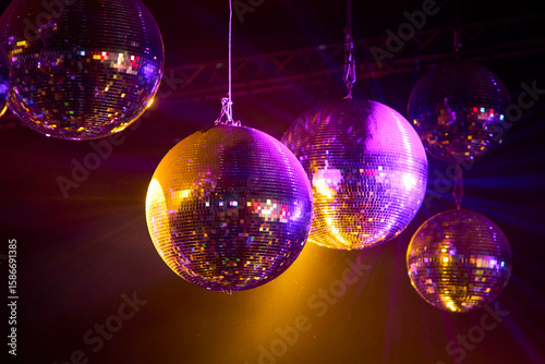 Tableau sur toile Fotografía de 5 bolas disco colgantes iluminadas con luces de colores rosados y amarillos, en un entorno oscuro tipo club nocturno