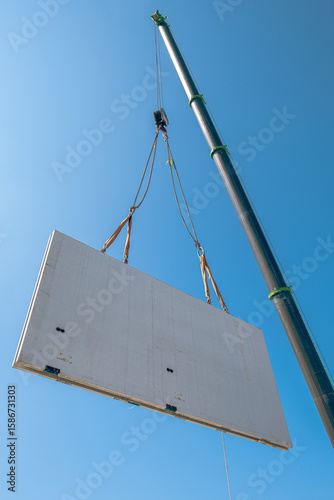 Prefabricated concrete wall being lifted by crane at construction site