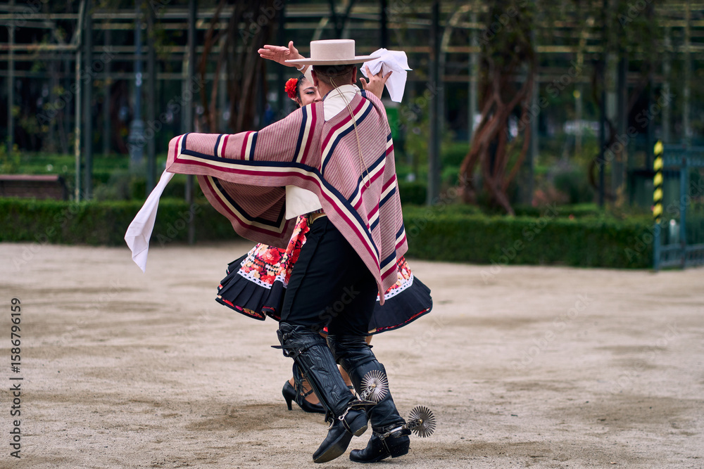Fototapeta premium Portrait of a smiling young couple dressed as Chilean huasos, posing and joyfully dancing cueca outdoors. Traditional Chilean dance. Chilean traditions, celebrations, and culture.