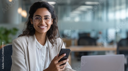 Young Indian business woman manager ceo using cell phone mobile app laptop. Smiling Latin Hispanic mature female businesswoman holding smartphone in office trading, reading, working online.