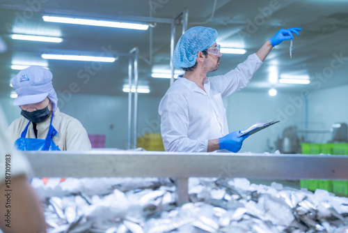Εκτύπωση καμβά A supervisor in a food processing plant wearing protective gear, inspecting a fish while holding a clipboard, emphasizing quality control, hygiene, and safety in the seafood production process