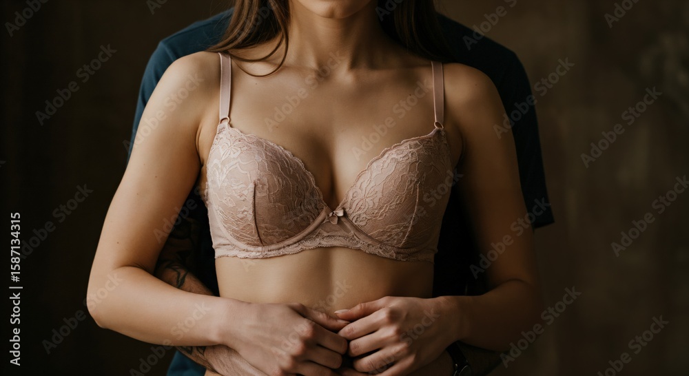 Fototapeta premium Man hugging a woman in a lace bra from behind. Intimate and sensual moment between a young couple. Close up on the embrace.