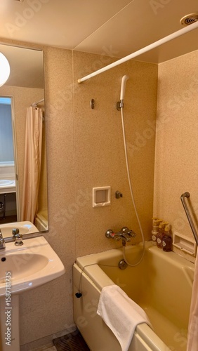 Vertical image of a typical small Japanese bathroom with sink and bath with shower inside a hotel room during a holiday in Japan.
