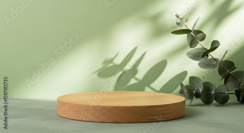 A minimalist display podium made of wood sits on a green surface with eucalyptus leaves and soft shadows