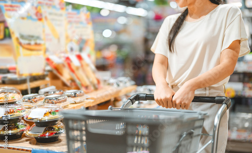 Young adult asian woman consumer choosing ready meals cooked food at supermarket store choice buying