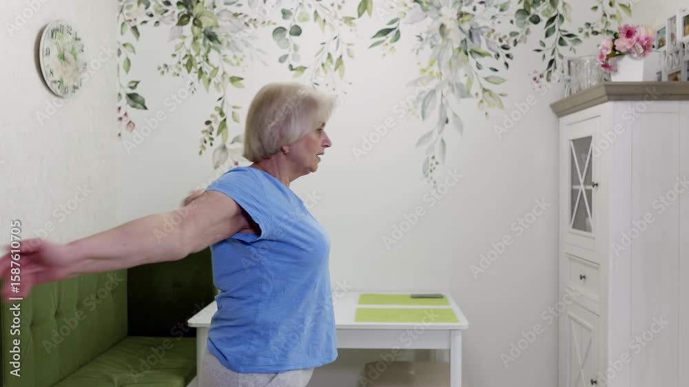 Senior woman stands in her dining room, performing a series of arm stretches, demonstrating her commitment to maintaining physical health and flexibility in her later years