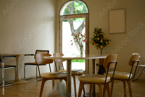 Cozy and minimalistic cafe interior with wooden chairs and a round table decorated with a vase of fresh flowers