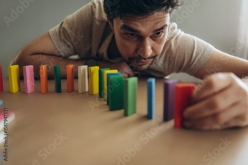 Man setting up colorful dominoes indoors for a chain reaction game