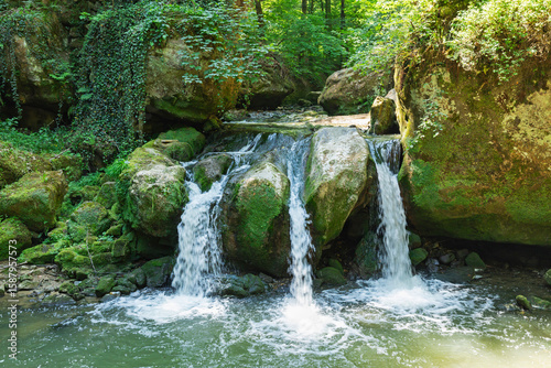 Schiessentuempel waterfall in Mullerthal, Luxembourg's Little Switzerland, surrounded by lush greenery and rocks.