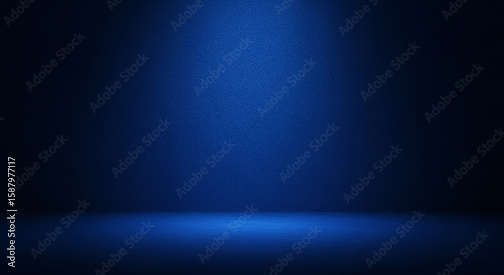 Obraz premium A spotlight illuminates a textured dark blue studio background creating a dramatic and moody atmosphere with a clear separation between floor and wall