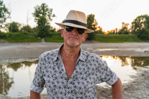 portrait of a smiling middle-aged man wearing a panama summer hat and sunglasses on the riverbank at sunset