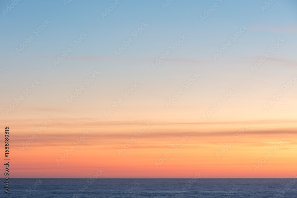 Sunset sky with an orange glow, light cloud and view across a calm ocean Sunset sky with an orange glow, light cloud and view across a calm ocean