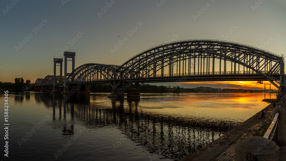 Naklejka premium Silhouette of Finlyandsky Railway Bridge over Neva River at sunset with reflection in water and orange sky. Saint Petersburg, Russia.