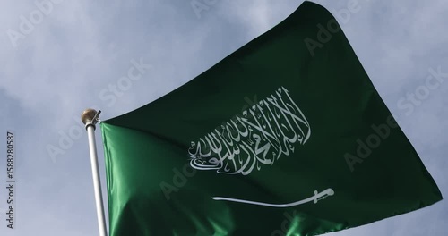 The Saudi Arabian flag is captured in close-up. The flag of Saudi Arabia, fluttering against the blue sky, is the national symbol of Saudi Arabia. Great for news.