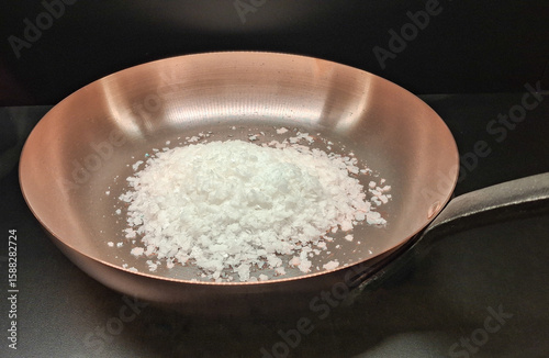salt flakes in a fry pan, on black background