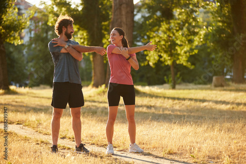 Two individuals perform dynamic stretching exercises in a sunlit park, promoting health and wellness through physical activity and engagement in nature.