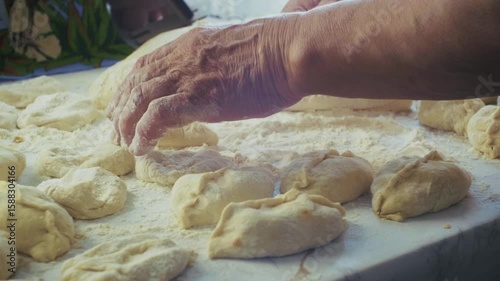 A hand is skillfully shaping dough on a floured surface amid neatly arranged pieces of uncooked pastry.