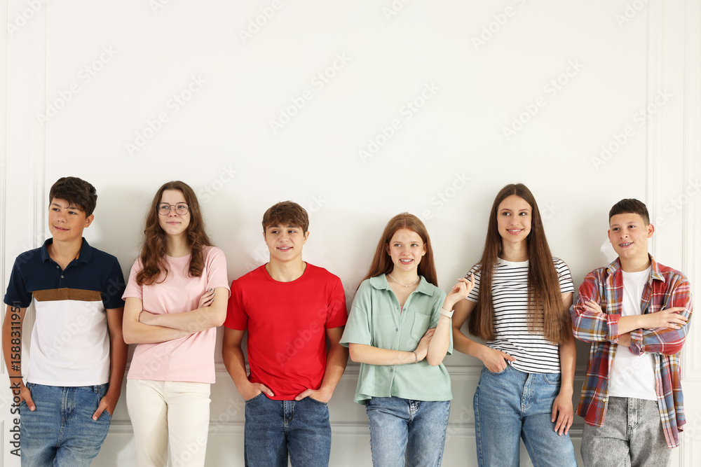 Group of happy teenagers posing near white wall indoors Group of happy teenagers posing near white wall indoors