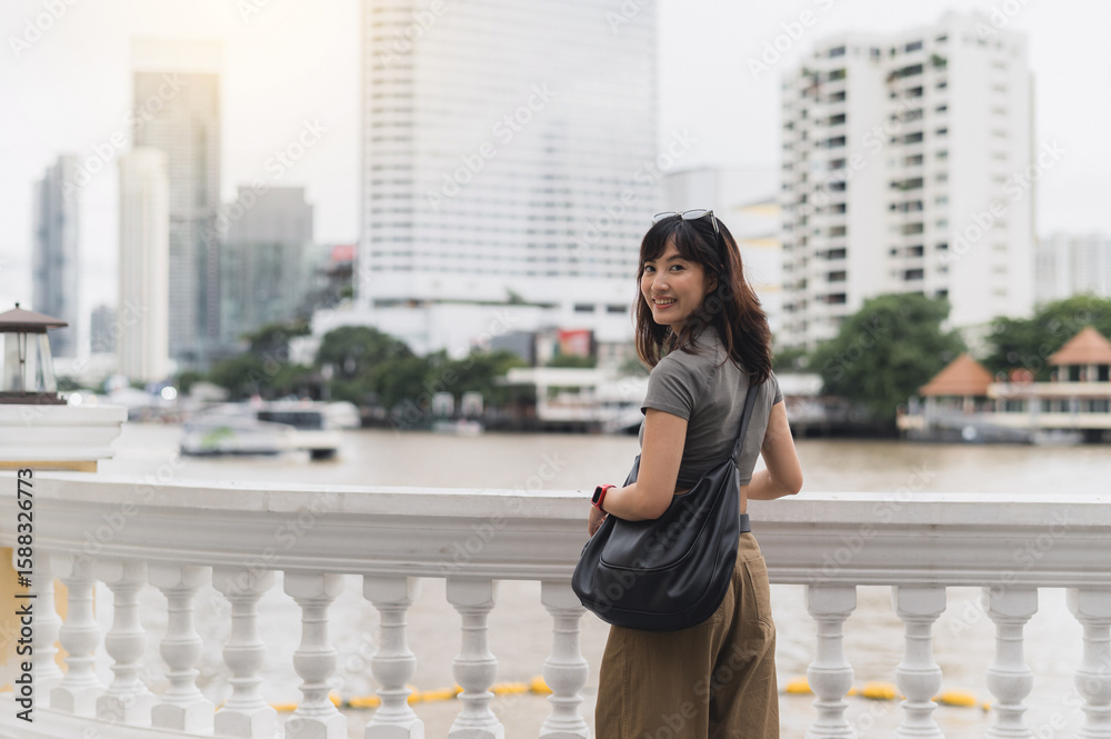 Fototapeta premium Happy solo southeast asian woman teenager blogger. World travel and asia tourism concept. Local cultural experience for explorer to wait for express boat on Chao Phraya River Bangkok Thailand