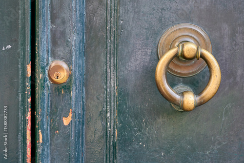 Close-up of an old, weathered green wooden door featuring a brass knocker and keyhole, highlighting its age and history.