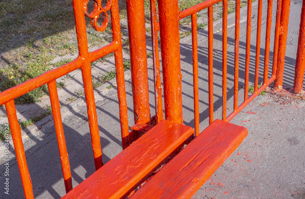 Bright orange bench and fence casting shadows on the sidewalk Bright orange bench and fence casting shadows on the sidewalk
