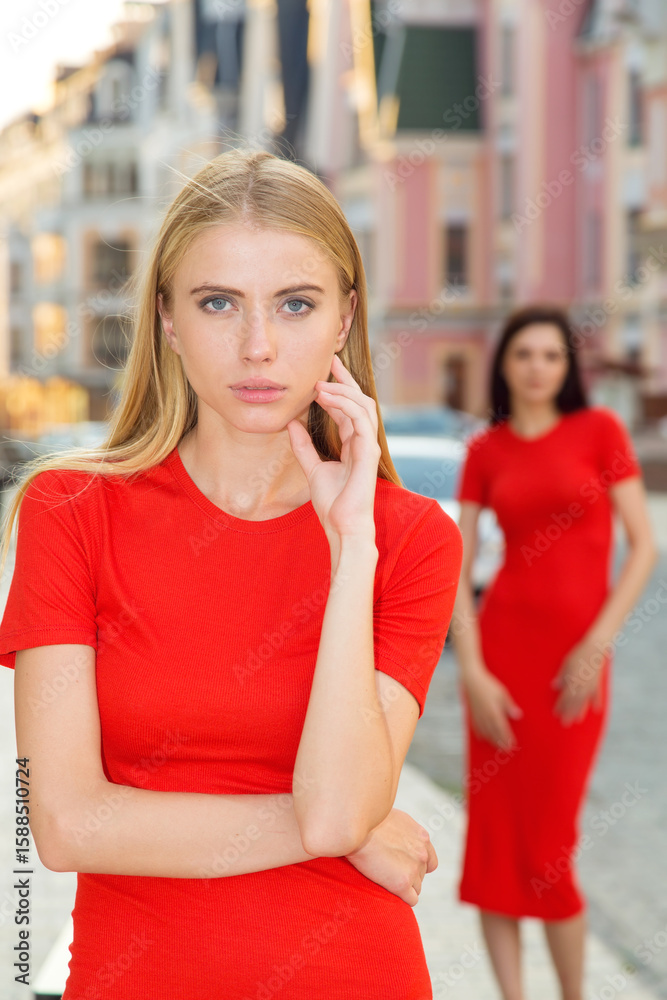 Fototapeta premium Two girls wearing fashionable dress. Women in red dress on a background of city streets.