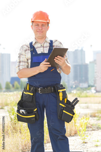 Male builder with electronic tablet in hands. Seating is on a new construction site. Male construction engineer with touch pad and checking building and site construction. Get important message.