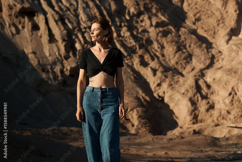 Naklejka premium A stylish woman poses confidently in a black top and jeans outdoors.