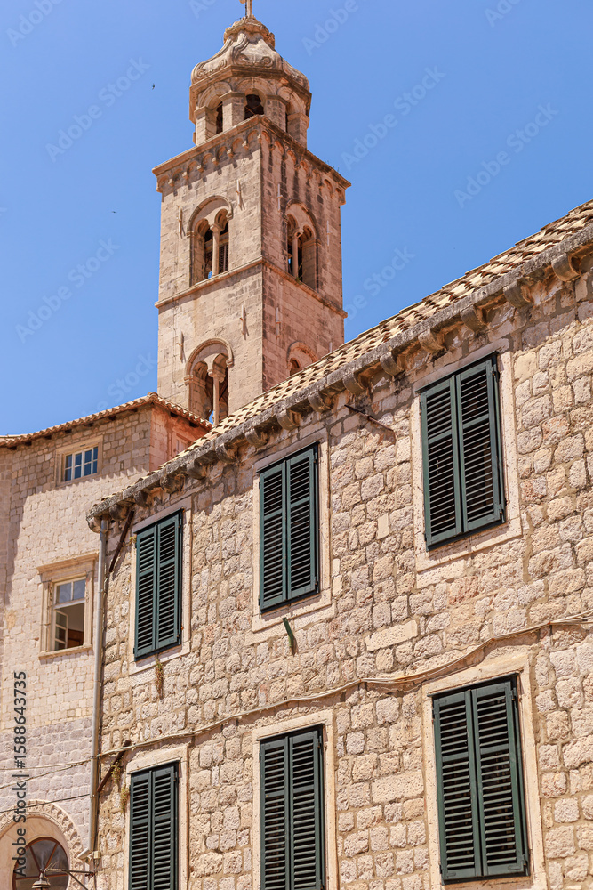 Bell tower rises above a historic stone building with dark green shutters in Dubrovnik Old Town. Bright sky offers copy space. Bell tower rises above a historic stone building with dark green shutters in Dubrovnik Old Town. Bright sky offers copy space.